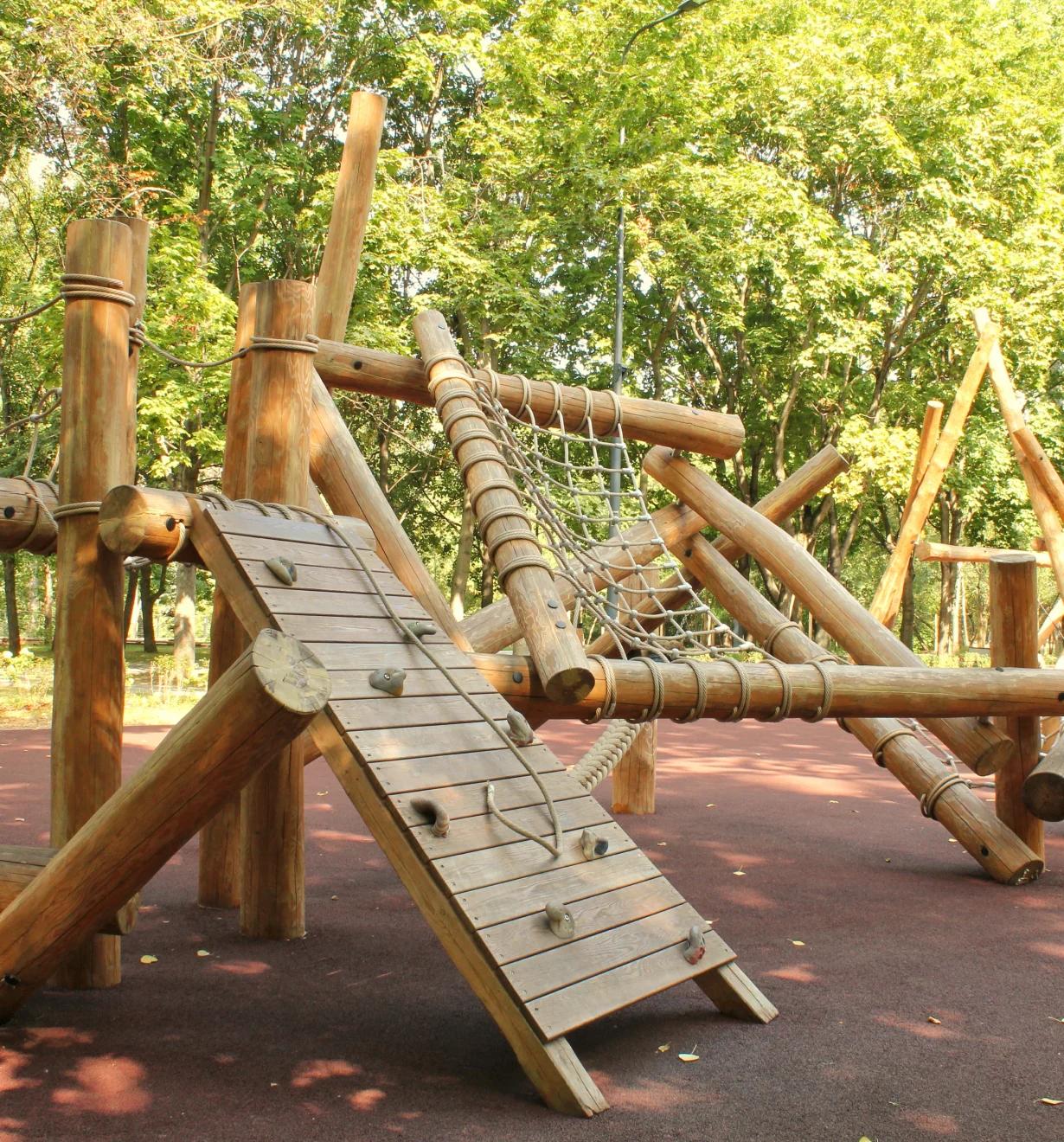 Log climbing frame with rope net and slatted wooden ramp on red rubber safety surfacing