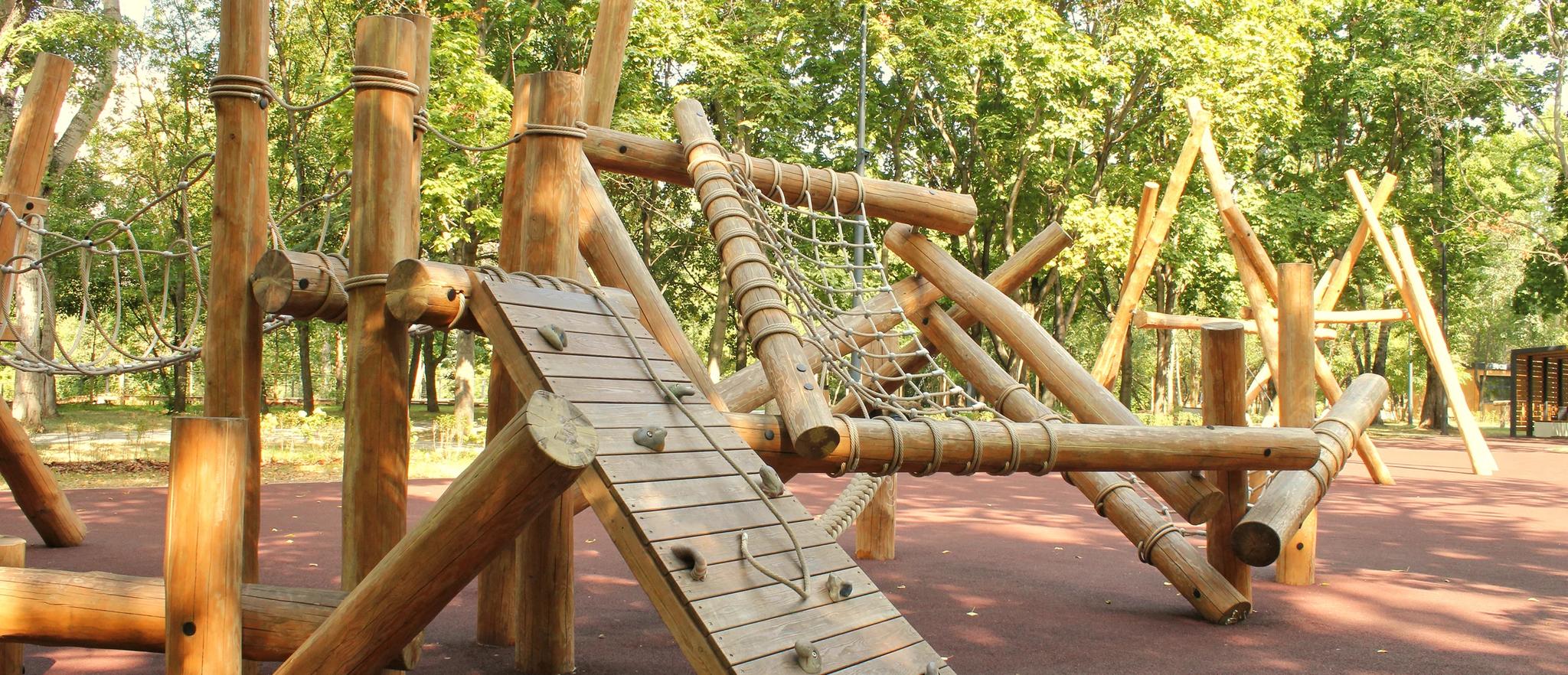 Log climbing frame with rope net and slatted wooden ramp on red rubber safety surfacing