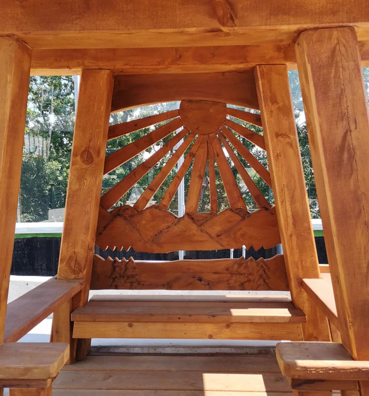 Timber frame with a carved sunburst panel and slatted bench seating